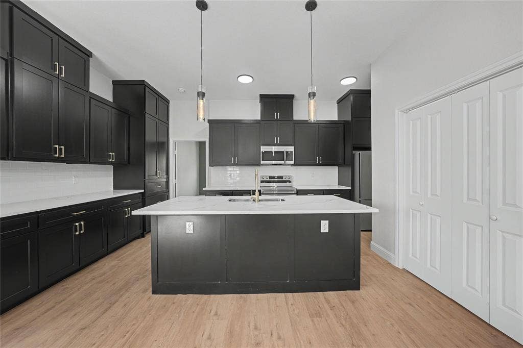 817 Stamps Avenue, Fort Worth, TX 76114 Modern kitchen featuring dark cabinetry, white countertops, stainless steel appliances, wood-finish flooring, and pendant lighting