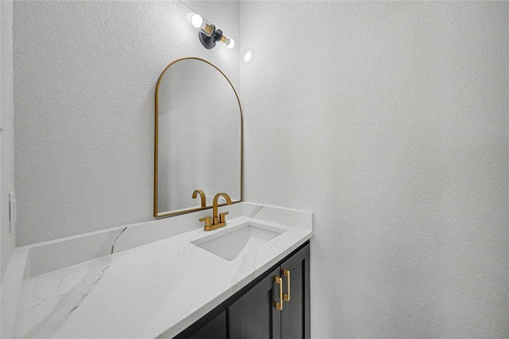 817 Stamps Avenue, Fort Worth, TX 76114 Half Bath Downstairs featuring a modern vanity with an integrated sink, white countertop with veining, matte black base cabinetry, and gold-finish hardware