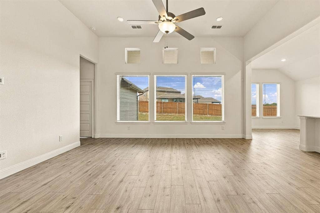 Vaulted ceilings featuring a central ceiling fan, wood-finish flooring, and expansive windows with transom detailing