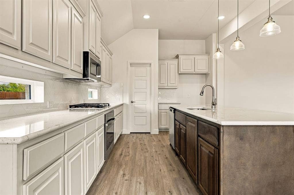 Kitchen featuring neutral cabinetry, light-toned countertops, wood-finish flooring, a stainless steel built-in microwave, and three glass pendant lights