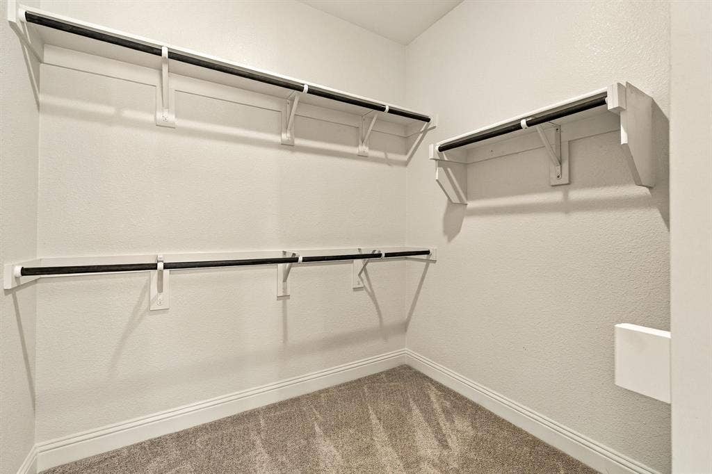Storage area featuring neutral carpeting and tiered white shelving with black garment rods
