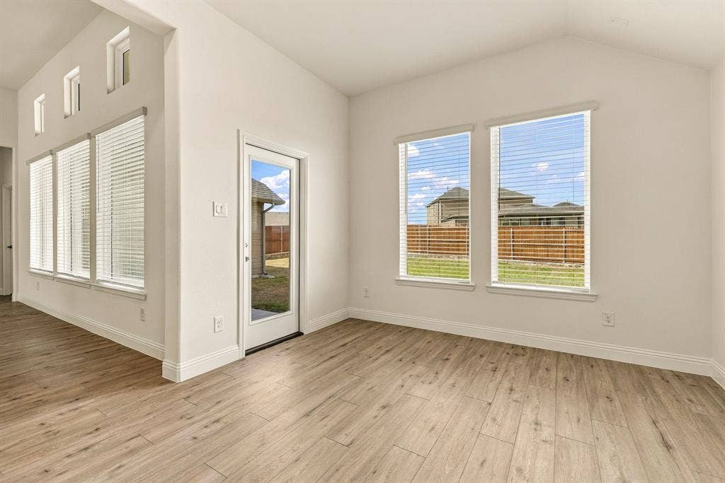 Vaulted ceilings featuring expansive windows, wood-finish flooring, and a glass-paneled exterior door