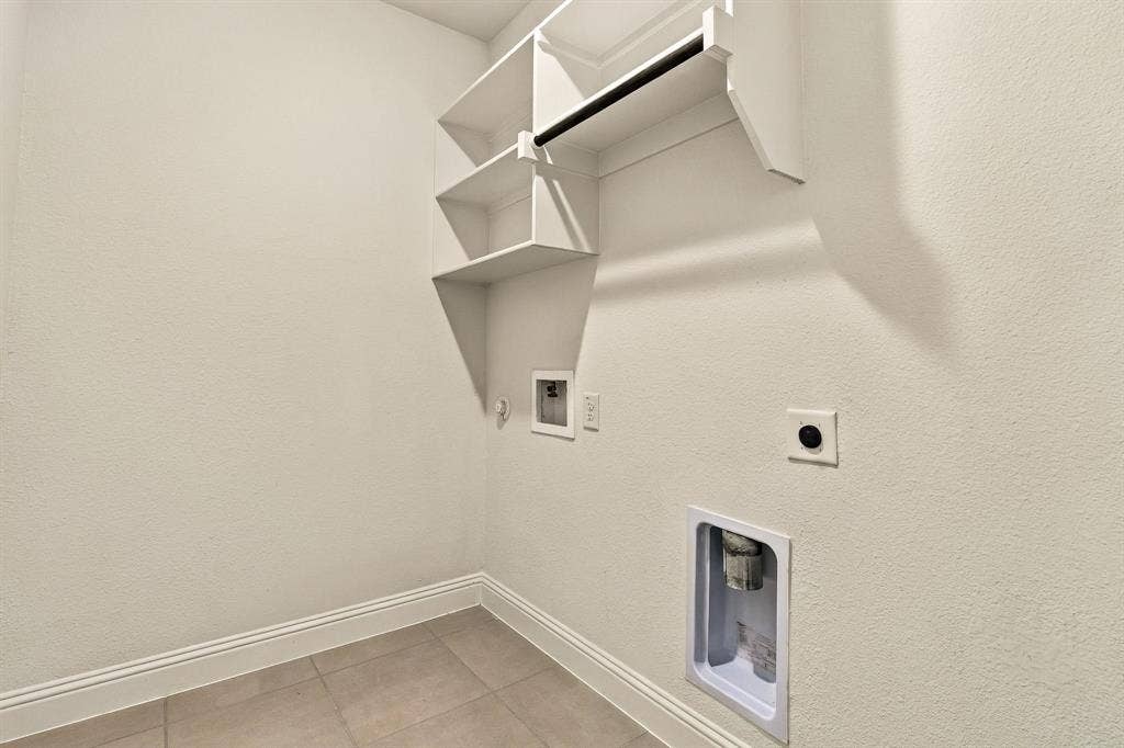 Utility space featuring neutral floor tiling, built-in shelving, a hanging rod, and dedicated washer and dryer hookups
