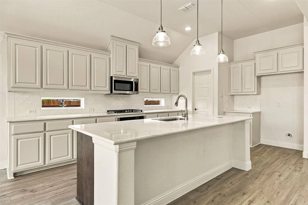Kitchen featuring light-toned cabinetry, a central island with stone-finish countertops, stainless steel appliances, wood-finish flooring, and glass pendant lighting