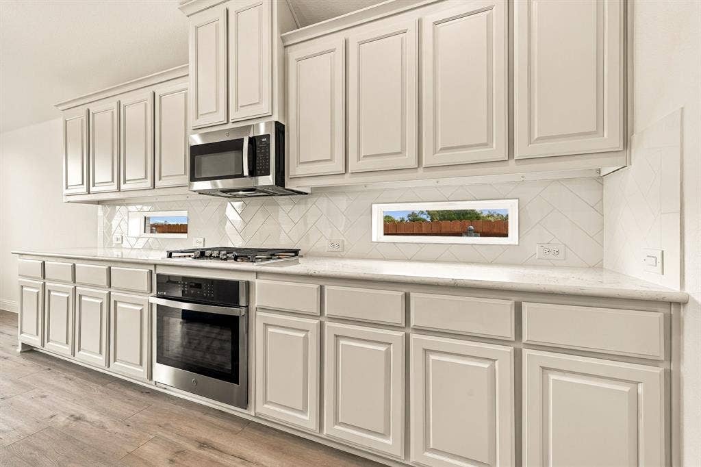 Kitchen featuring light-finish cabinetry, stone-surface countertops, herringbone-pattern tile backsplash, stainless steel built-in appliances, and wood-finish flooring