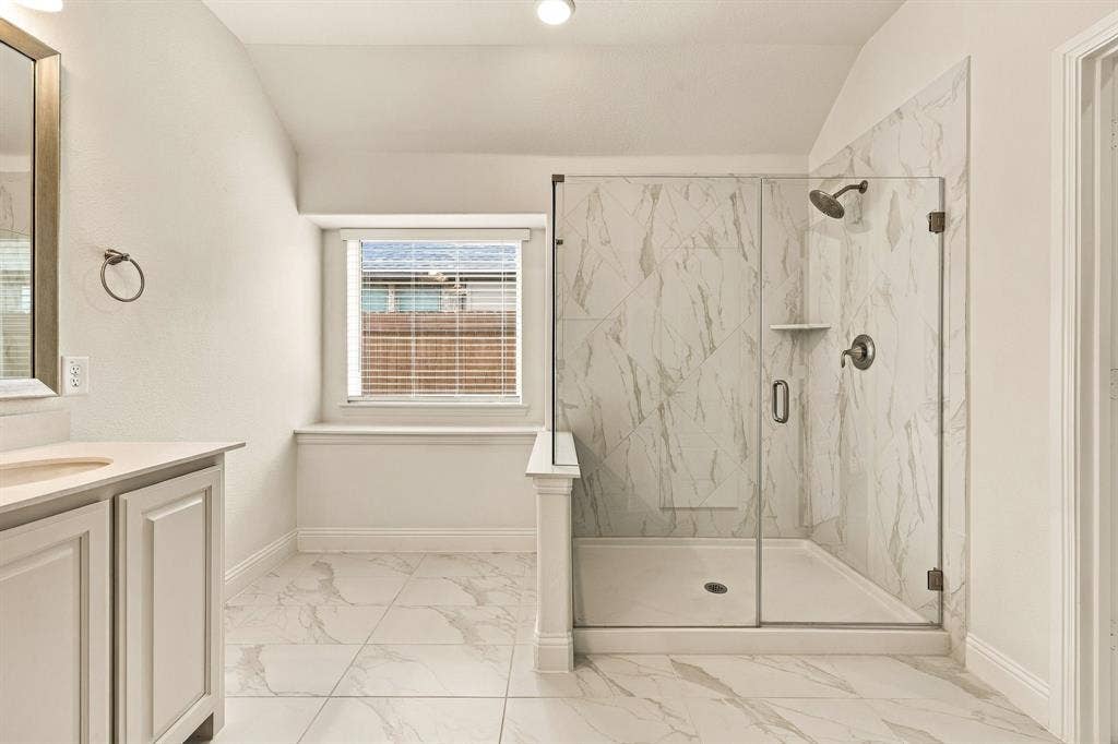 Walk-in glass-enclosed shower featuring large-format stone-patterned tile, white cabinetry with countertop, and matching floor tile
