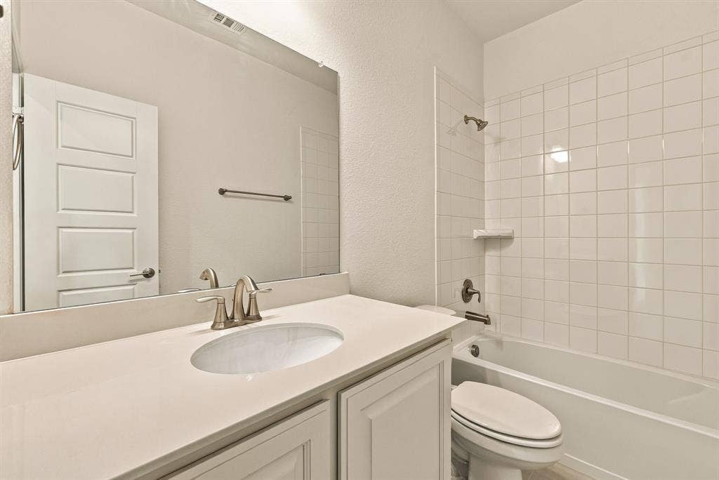 Bathroom featuring a vanity with a light-toned countertop, an undermount oval sink, a wall-to-wall mirror, and a tile-surround shower and tub combination