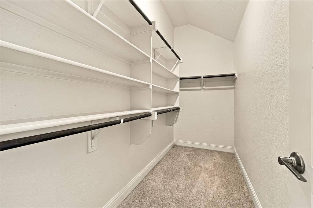 Walk-in closet featuring tiered white shelving, integrated hanging rods, and carpeted flooring