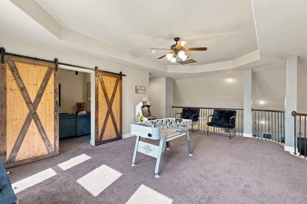 Generously sized entertainment space featuring natural light, plush carpeting, and rustic sliding barn doors leading into the adjoining media room.