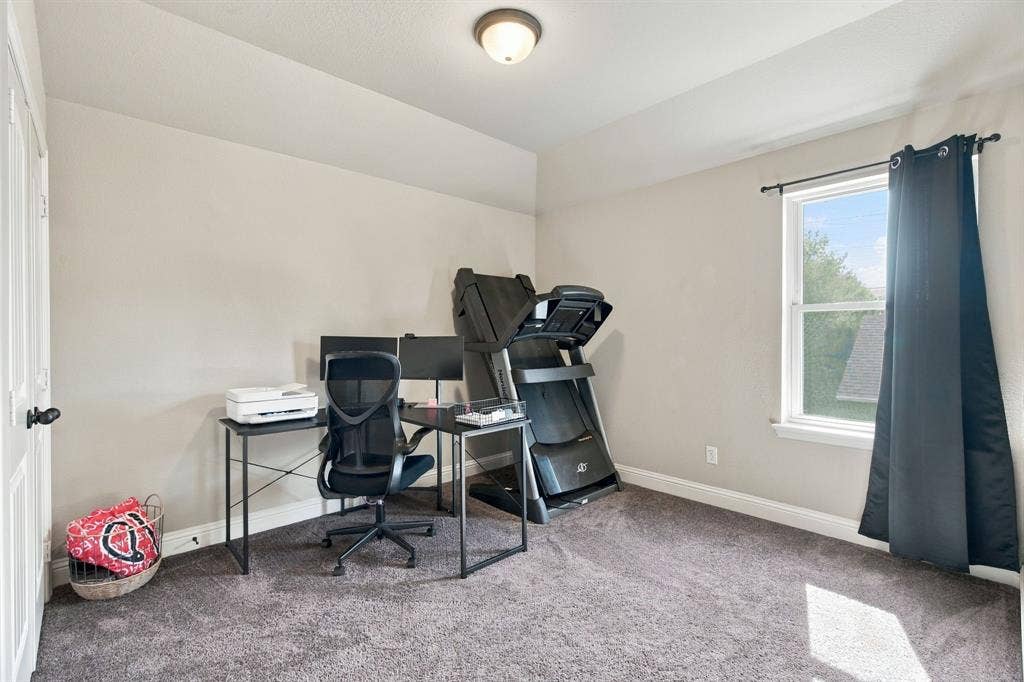 Versatile upstairs bedroom currently used as a home office and exercise space, featuring a large window, ceiling fan, and flexible floor space.