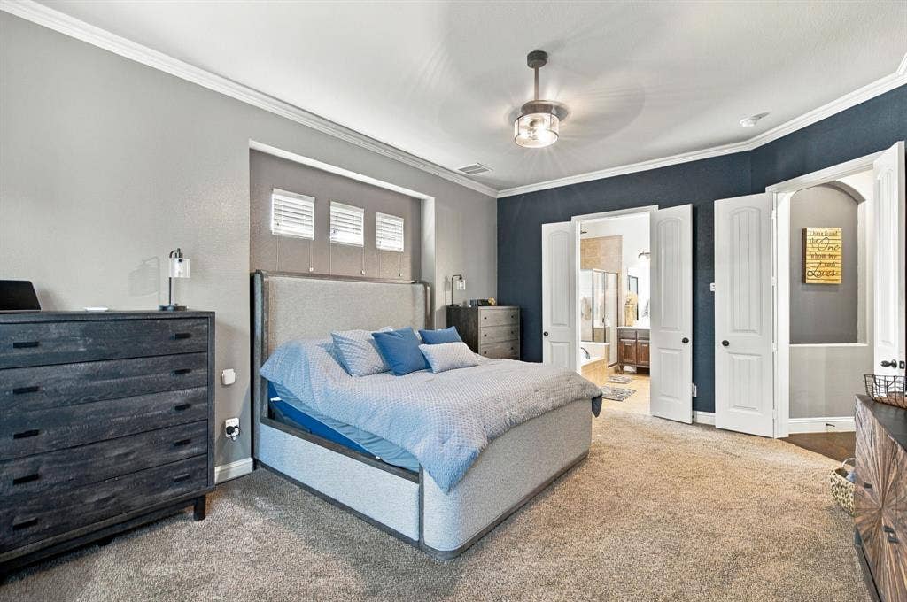 Another view of the generously sized primary bedroom highlights the tray-style wall recess behind the bed, contrasting accent walls, and direct access to the ensuite bathroom.