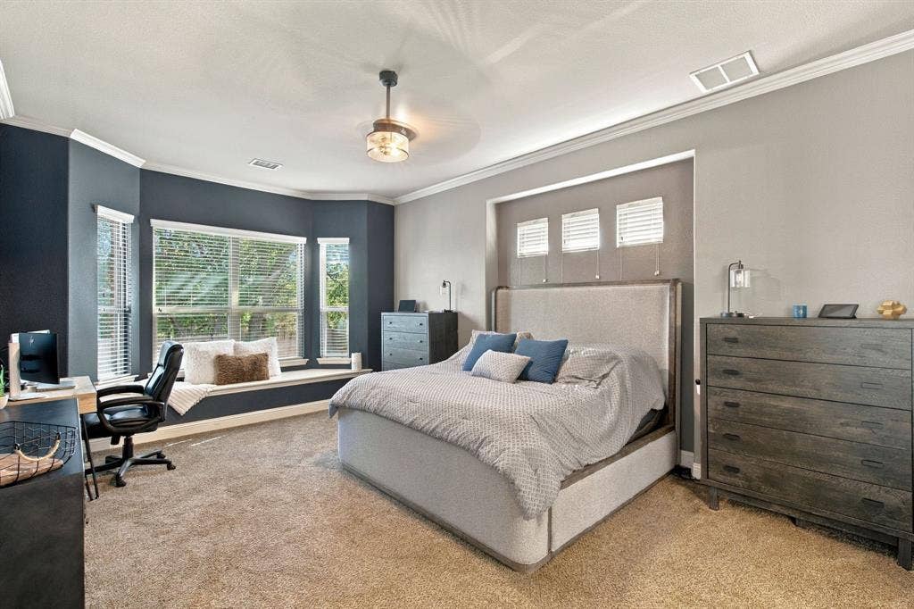 Spacious downstairs primary suite featuring a large bay window with built-in window seating, crown molding, and plenty of room for a king-sized bed and additional furnishings.