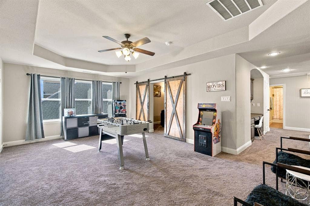 Spacious upstairs flex area with tray ceiling, ceiling fan, and multiple windows, offering plenty of room for games, recreation, or a second living space.