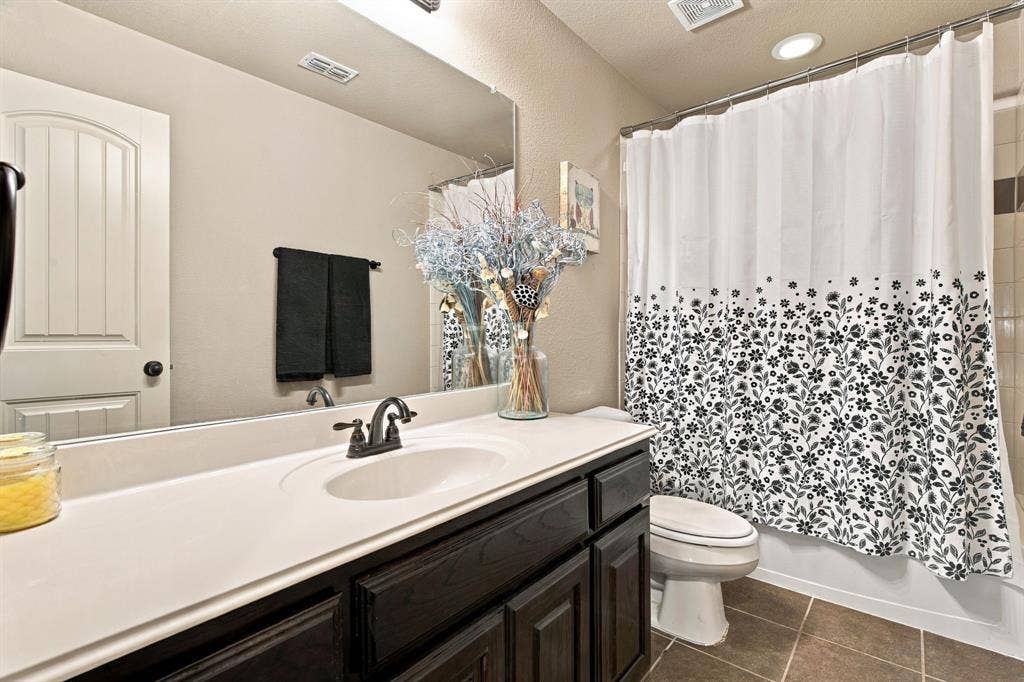 Additional upstairs bathroom with a tub-shower combination, dark wood cabinetry, spacious vanity countertop, and tile flooring.