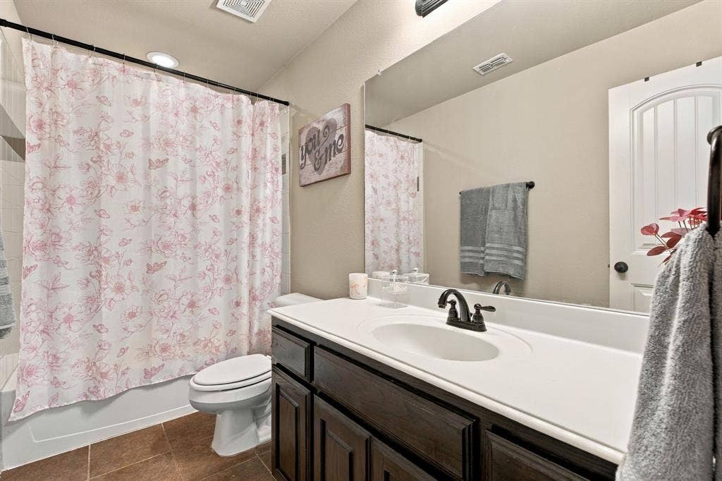 Upstairs full bathroom featuring a tub-shower combination, dark wood vanity, generous countertop space, and a large wall mirror.