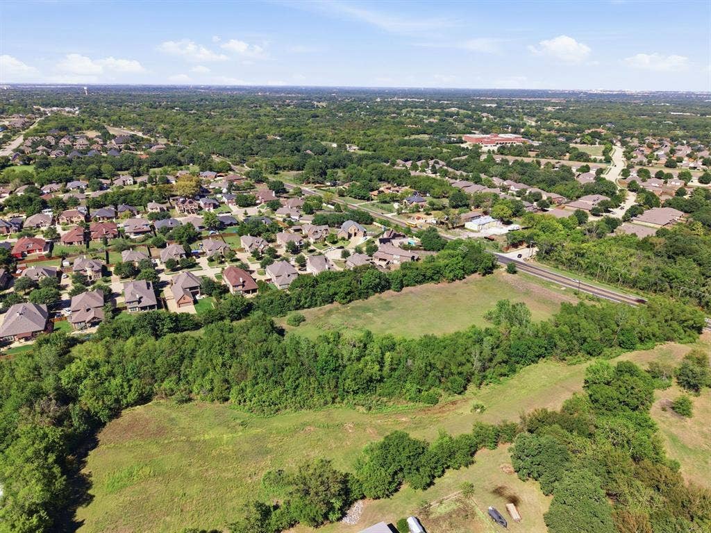 Aerial perspective highlighting the established neighborhood, spacious surroundings, and dense tree coverage behind the homes.