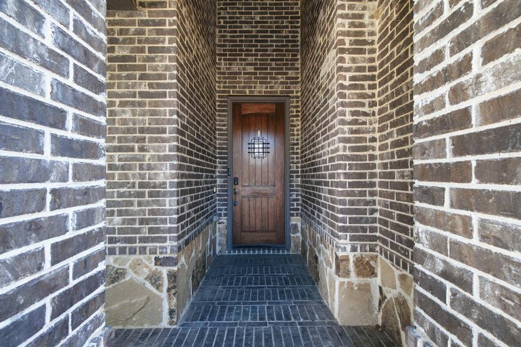 Recessed entryway featuring rich brick and stone detailing, brick paver flooring, and a handsome wood front door.