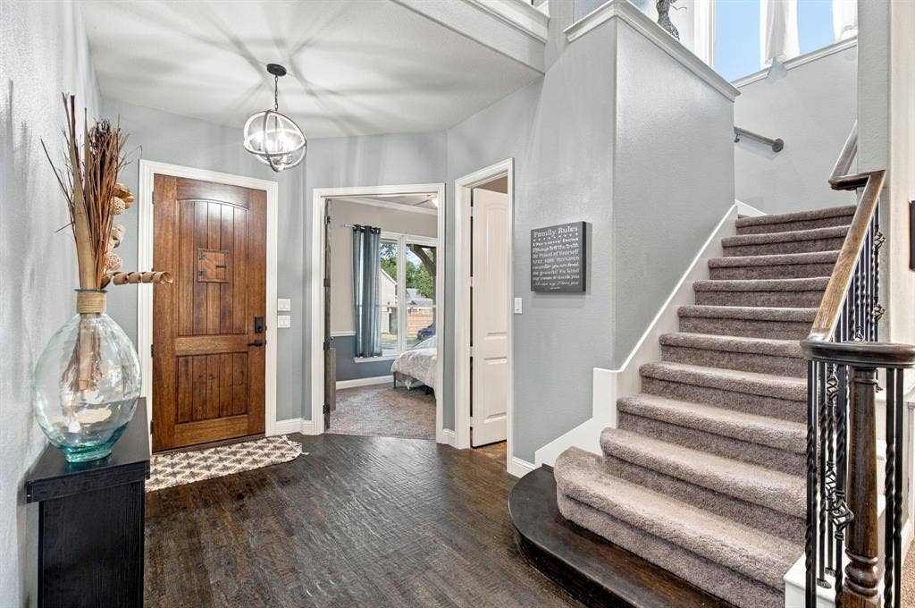 Welcoming foyer with a rich wood front door, dark flooring, statement pendant lighting, and a curved staircase with decorative iron balusters.