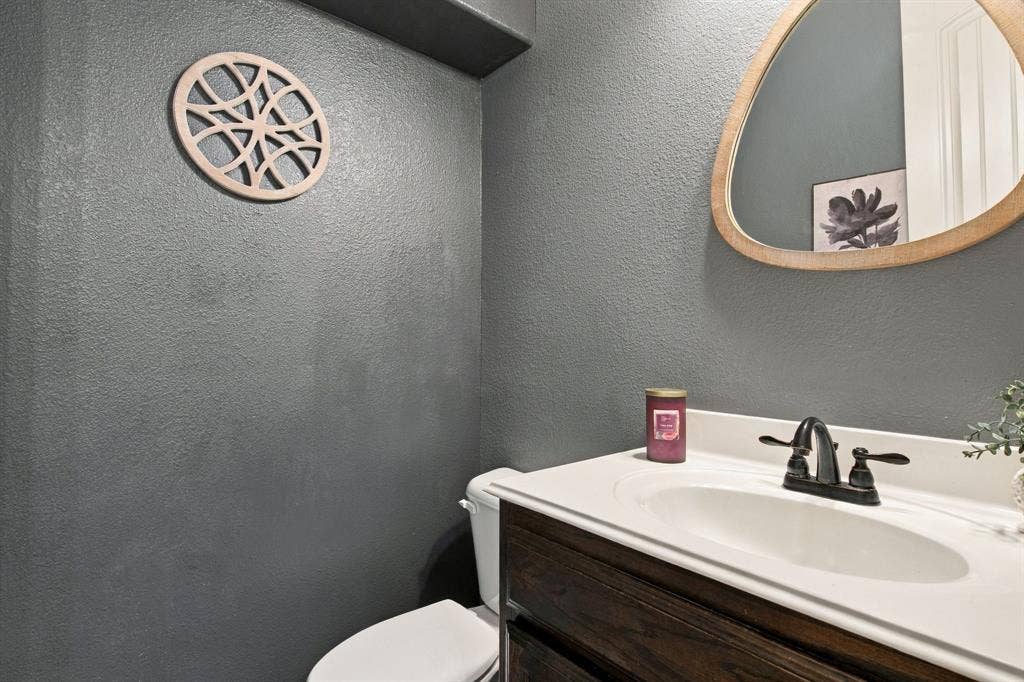 Convenient downstairs half bath featuring a dark wood vanity, white countertop, contrasting charcoal walls, and a decorative mirror.
