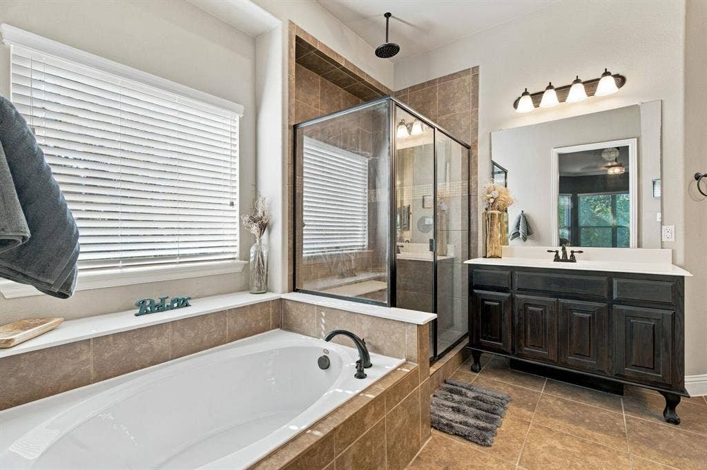 A closer look at the primary bathroom's separate soaking tub and glass-enclosed shower, featuring decorative tile accents, a rainfall-style showerhead, and a built-in shower bench.