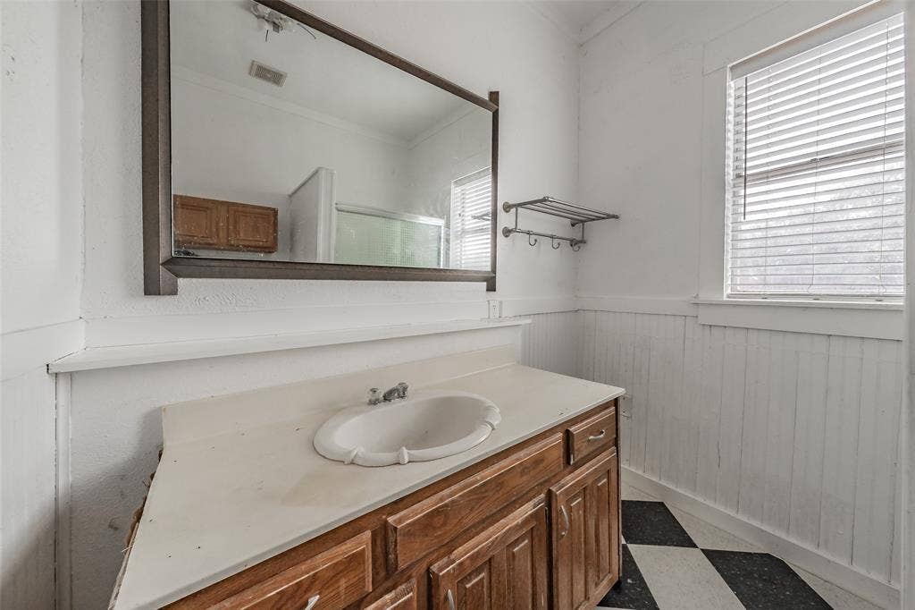 212 N Ruddell Street, Denton, TX 76205 Wood-finish vanity with an integrated sink, large wall mirror, and a window with horizontal blinds