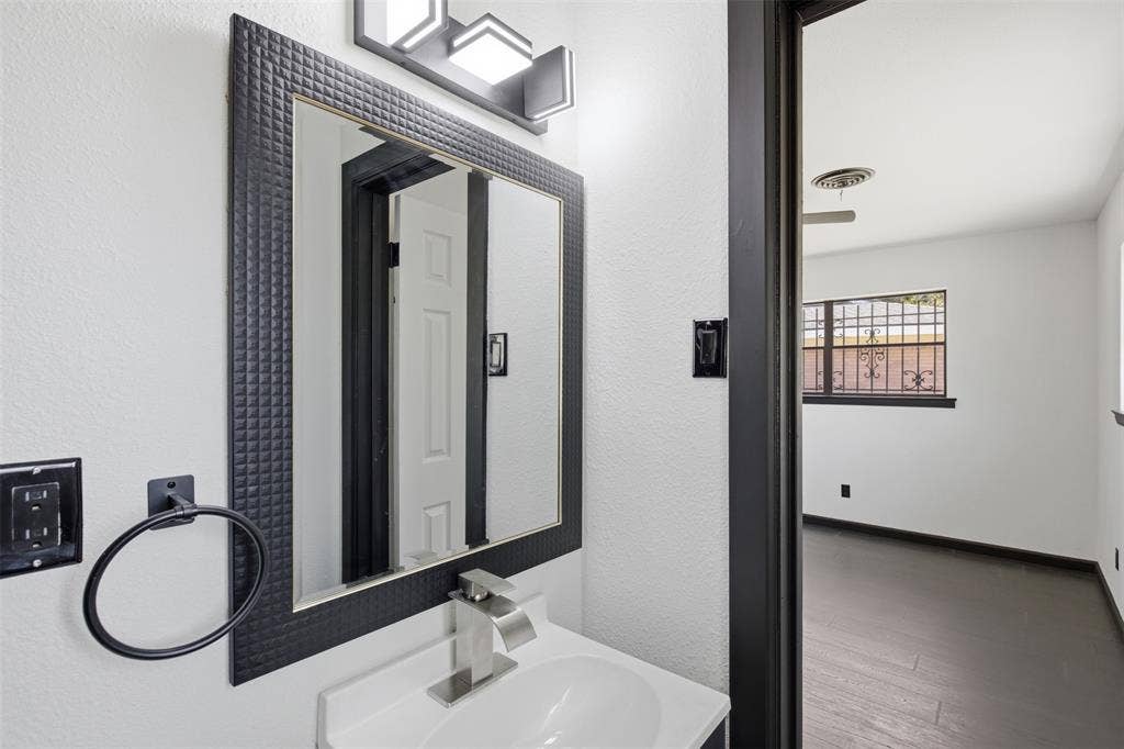 2313 Clearview Drive, Fort Worth, TX 76119 Vanity featuring a white basin sink, brushed nickel faucet, and a textured black-framed mirror