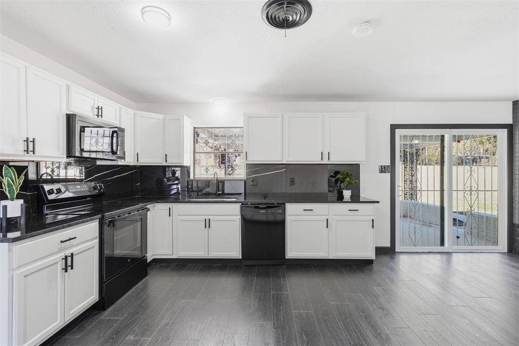 2313 Clearview Drive, Fort Worth, TX 76119 White cabinetry with dark hardware, dark stone countertops, dark backsplashes, dark wood-finish flooring, and a sliding glass door