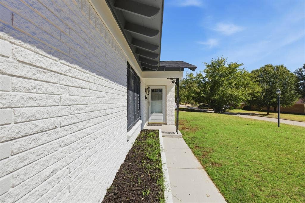 2313 Clearview Drive, Fort Worth, TX 76119 White brick exterior, black wrought iron window security bars, covered entry, concrete walkway, and manicured lawn