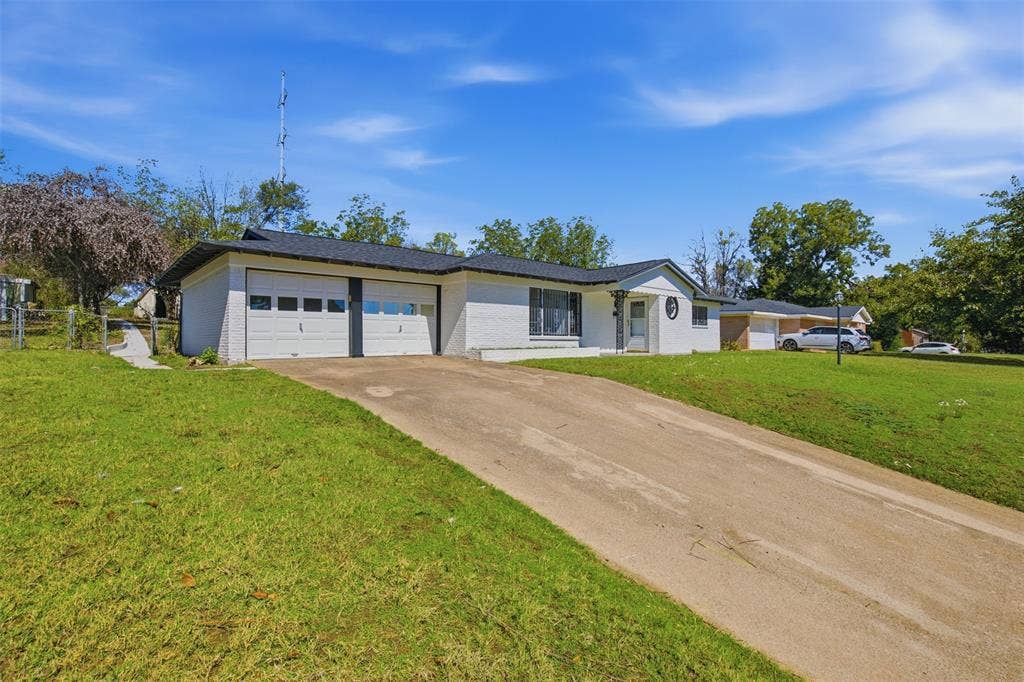 2313 Clearview Drive, Fort Worth, TX 76119 White painted brick exterior with a dark shingle roof, two-car garage with panel doors and window inserts, and an extensive concrete driveway