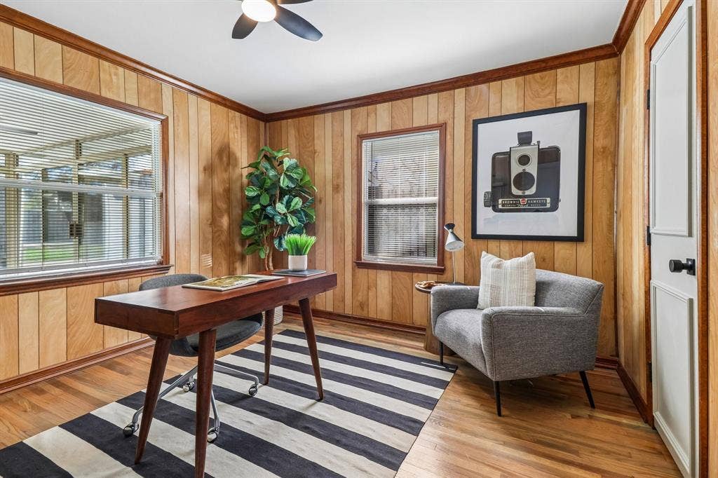 Wood-paneled room featuring wood-finish flooring, a ceiling fan, and multiple windows