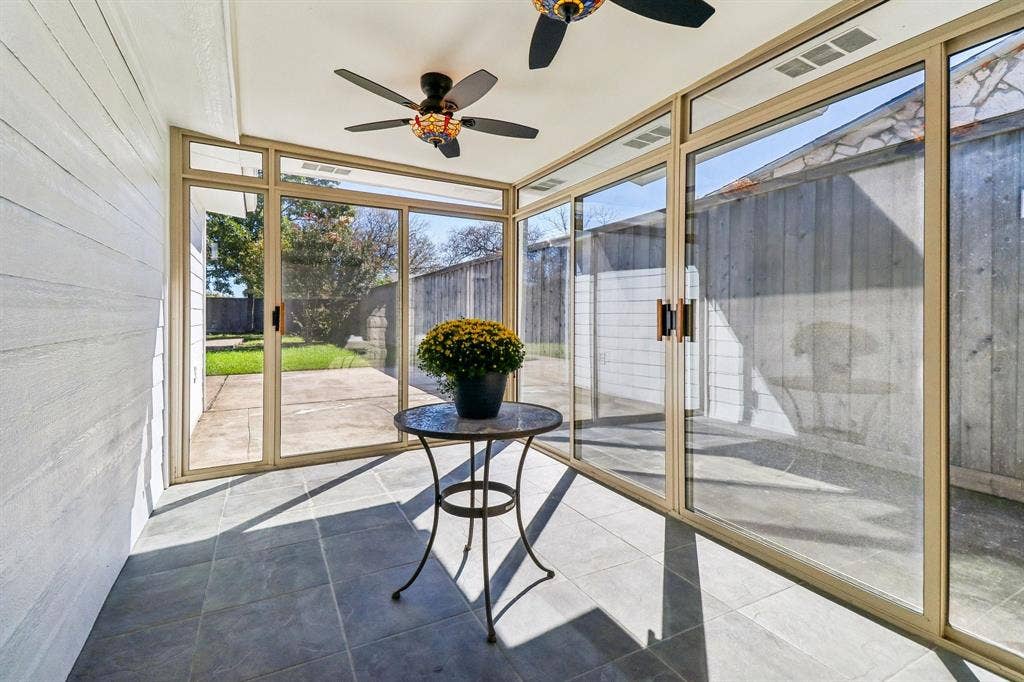 Sunroom featuring full-height sliding glass doors, tile flooring, two ceiling fans, and wood-paneled walls