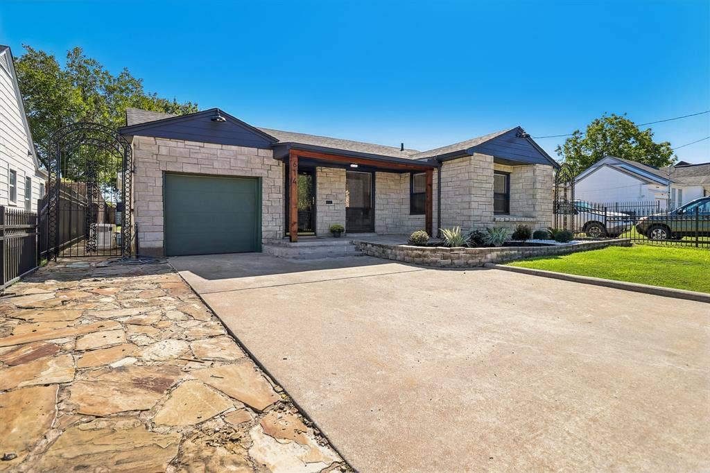 Stone facade exterior with a covered entry, concrete driveway, and a flagstone pathway