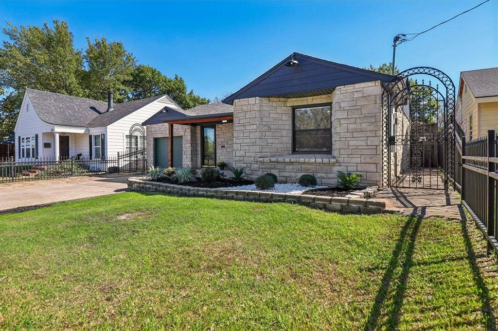 Stone veneer exterior, dark-colored roof, decorative wrought iron gate, front planter box with landscaping, paved driveway
