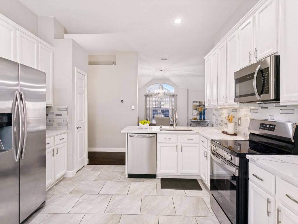 Kitchen featuring white cabinetry, light-toned tile flooring, stainless steel appliances, and a tiled backsplash