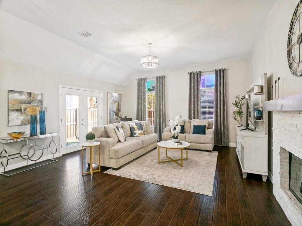 Vaulted ceiling with a chandelier, dark wood-finish flooring, double French doors, and a stone-clad fireplace
