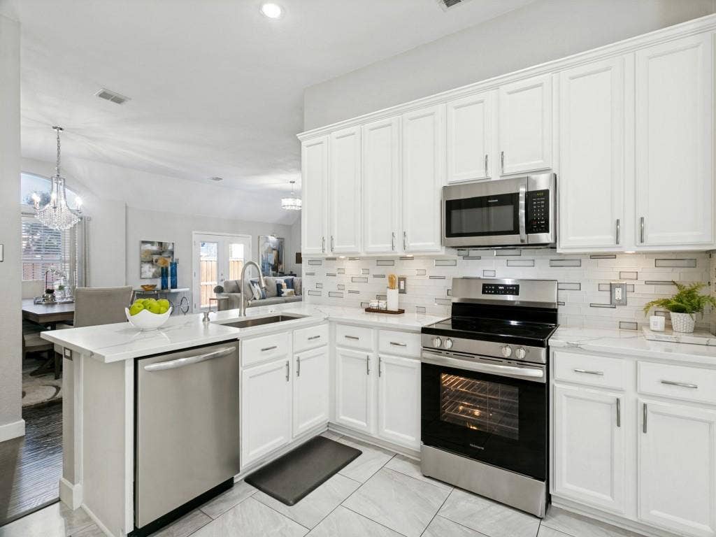 White cabinetry with stainless steel hardware, undermount kitchen sink, stainless steel appliances, patterned tile backsplash, and light-toned tile flooring