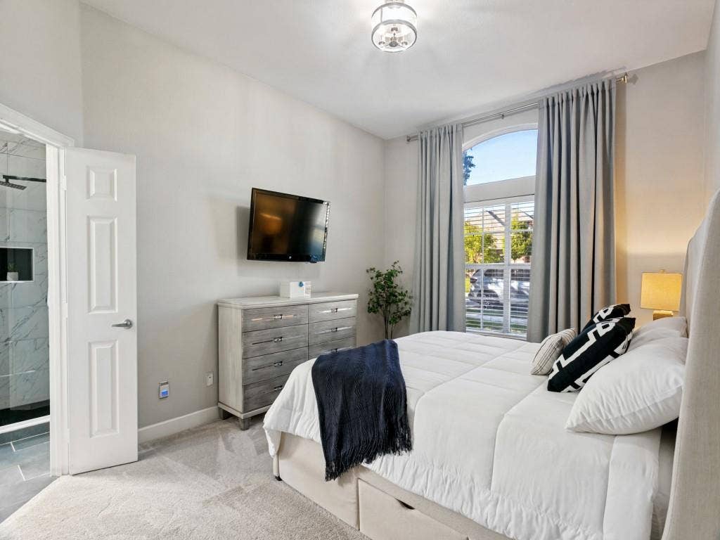 Recessed ceiling light fixture, arched window, carpet flooring, and an adjoining bathroom with tiled shower walls
