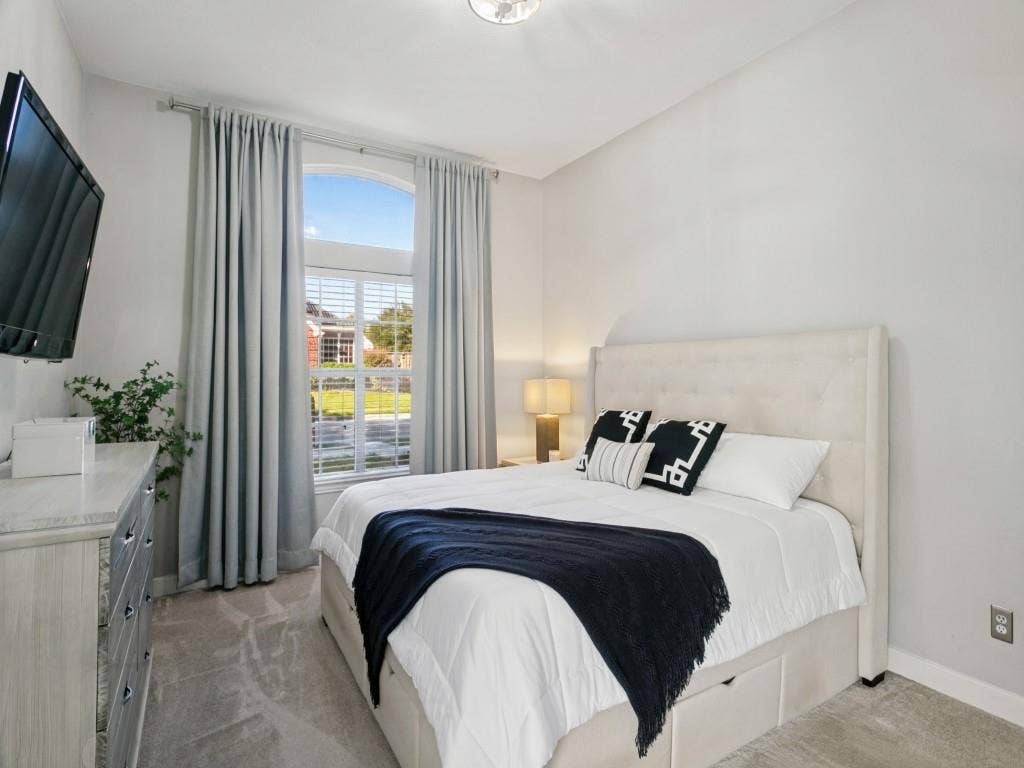 Arch-top window, wall-mounted television, recessed lighting fixture, light-toned wall paint, and gray carpet