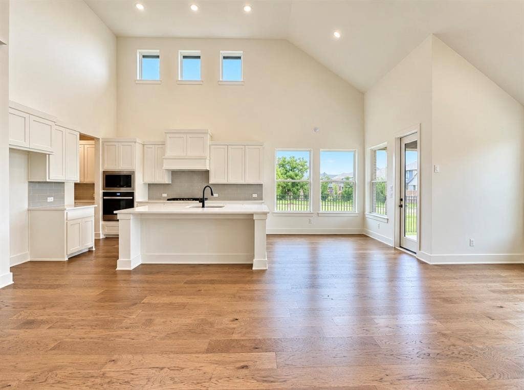 1129 Bradford Street, Celina, TX 75009 Vaulted ceiling with recessed lighting, wood-finish flooring, white cabinetry, integrated stainless steel appliances, and a central island with a sink