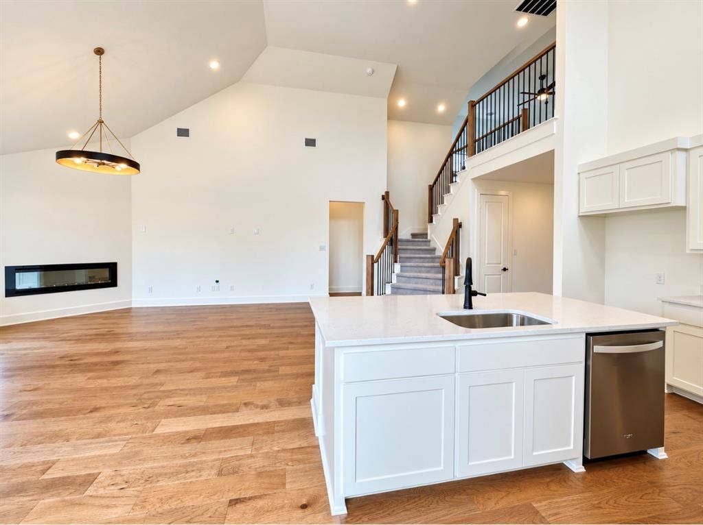 1129 Bradford Street, Celina, TX 75009 Open-concept living space featuring vaulted ceilings, wood-finish flooring, a modern linear fireplace, and a kitchen island with an integrated sink