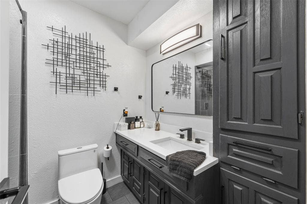 6606 Coleshire Drive, Dallas, TX 75232 White vanity countertop with an integrated sink, dark wood-finish cabinetry, and matte black fixtures