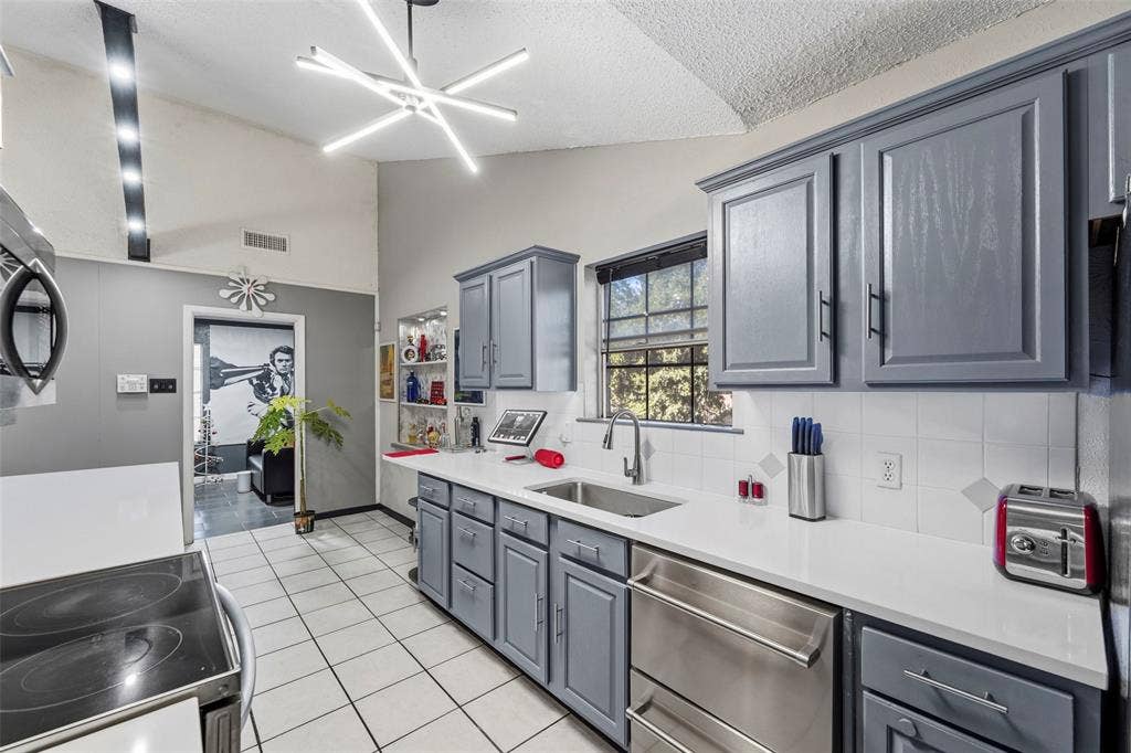 6606 Coleshire Drive, Dallas, TX 75232 Vaulted ceiling, contemporary linear chandelier, shaker-style cabinetry, white countertops, and stainless steel appliances