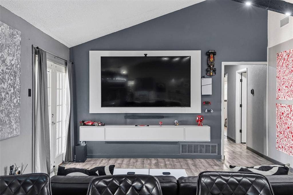 6606 Coleshire Drive, Dallas, TX 75232 Vaulted ceiling, wood-finish flooring, white double French doors, white framed media wall, and a floating entertainment console