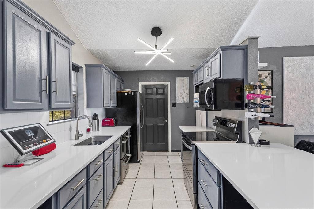 6606 Coleshire Drive, Dallas, TX 75232 Galley kitchen with white tile flooring, gray cabinetry, white countertops, built-in stainless steel appliances, and a modern ceiling light fixture