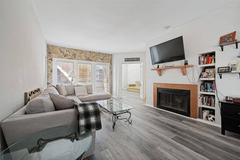 5550 Spring Valley Road, #C21, Dallas, TX 75254 Wood-finish flooring, built-in shelving, stone accent wall, fireplace with tile surround, and direct outdoor access