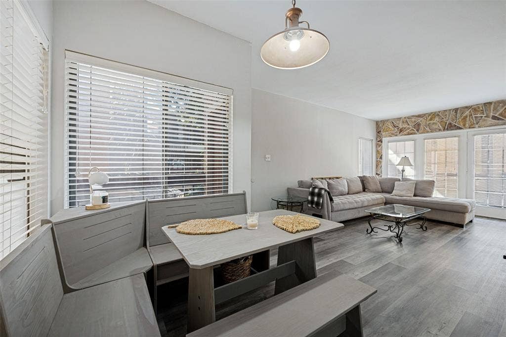 5550 Spring Valley Road, #C21, Dallas, TX 75254 Wood-finish flooring throughout, vaulted ceiling, built-in banquette seating, stone accent wall, and multiple window panels