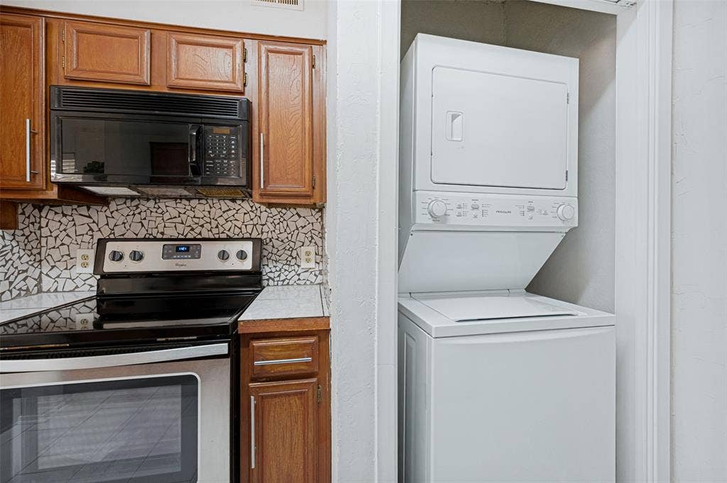 5550 Spring Valley Road, #C21, Dallas, TX 75254 Wood cabinetry, mosaic tile backsplash, stainless steel range with overhead microwave, and a stacked washer/dryer unit