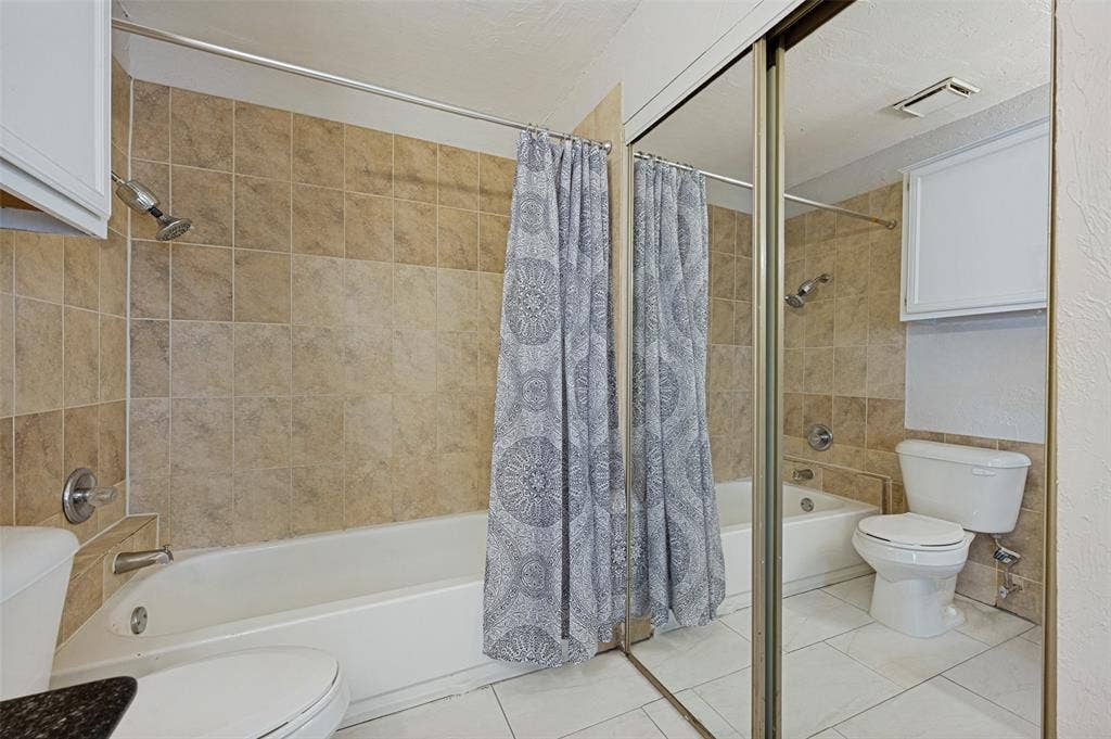 5550 Spring Valley Road, #C21, Dallas, TX 75254 Full-sized bathtub with a shower fixture, tile surround, white vanity cabinetry, and mirrored closet doors