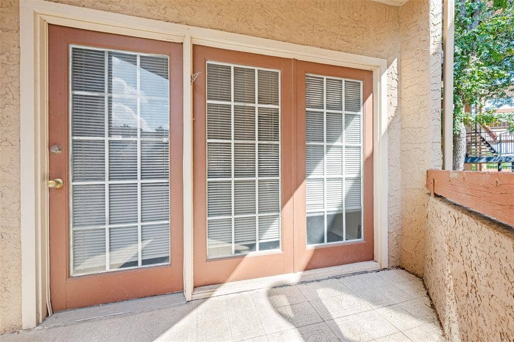 5550 Spring Valley Road, #C21, Dallas, TX 75254 Back balcony double doors with grid-patterned glass, an exterior wall with stucco finish, and a tiled patio surface