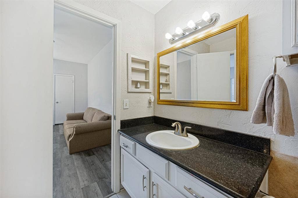 5550 Spring Valley Road, #C21, Dallas, TX 75254 White vanity with brushed nickel hardware, dark speckled countertop, undermount sink with brushed nickel faucet, and a large mirror with a gold-tone frame